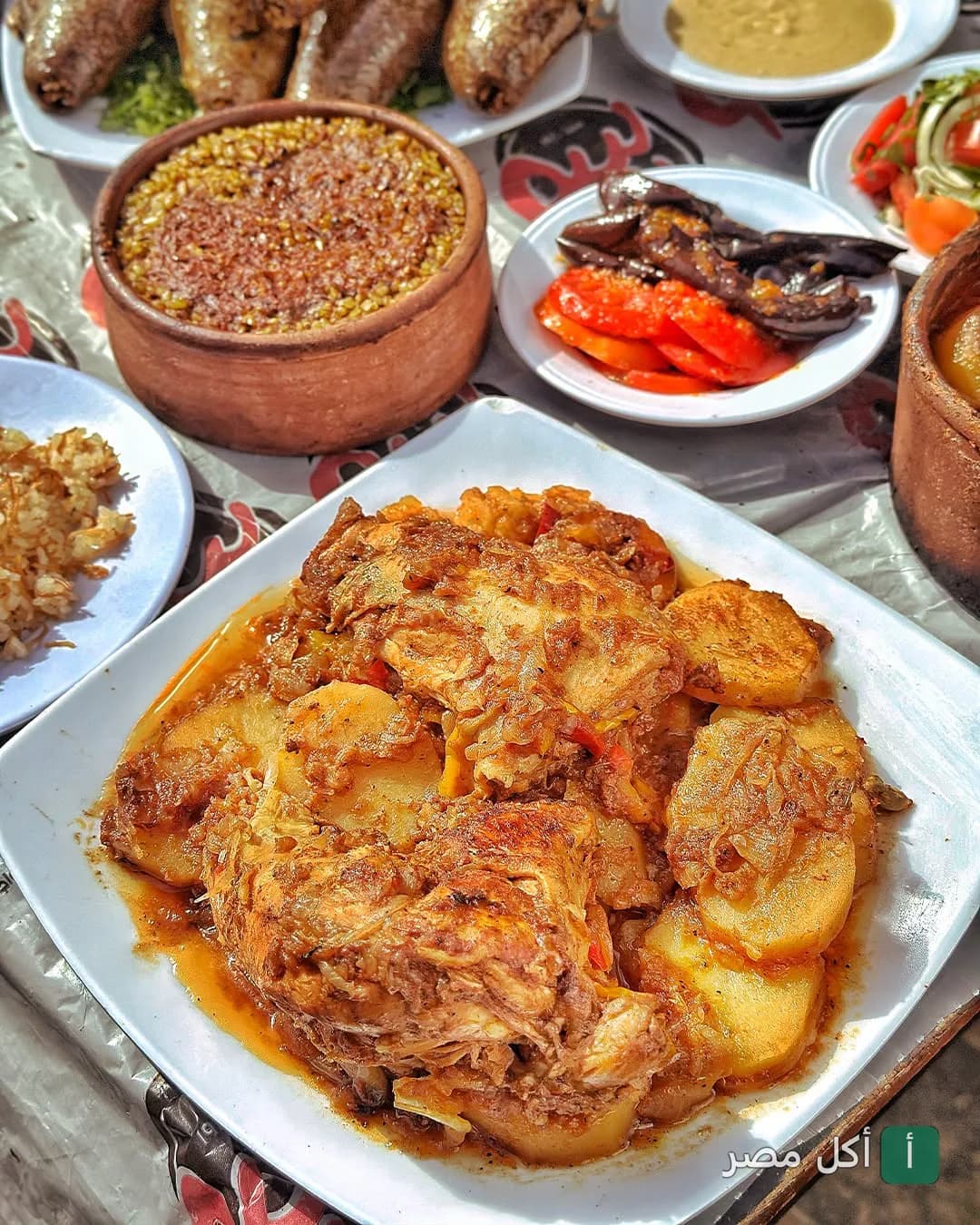 سفرة شرقية متنوعة من مطعم بيبو، تضم صينية بطاطس بالفراخ، طاجن أرز معمر، ومقبلات مثل الباذنجان المخلل.
