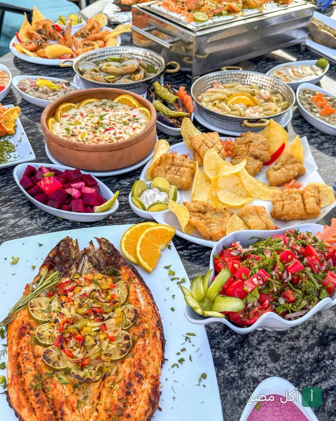 سفرة مأكولات بحرية متنوعة من مطعم أسماك المرشدي في العلمين، تشمل سمك مشوي ومقلي ومقبلات.