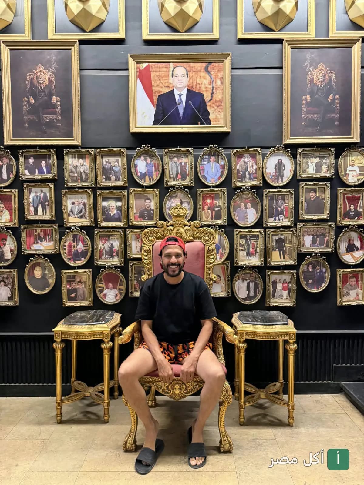 زبون يجلس على كرسي ذهبي مزخرف داخل مطعم قصر الكبابجي في الساحل الشمالي، مع حائط مزين بالعديد من الصور المؤطرة.
