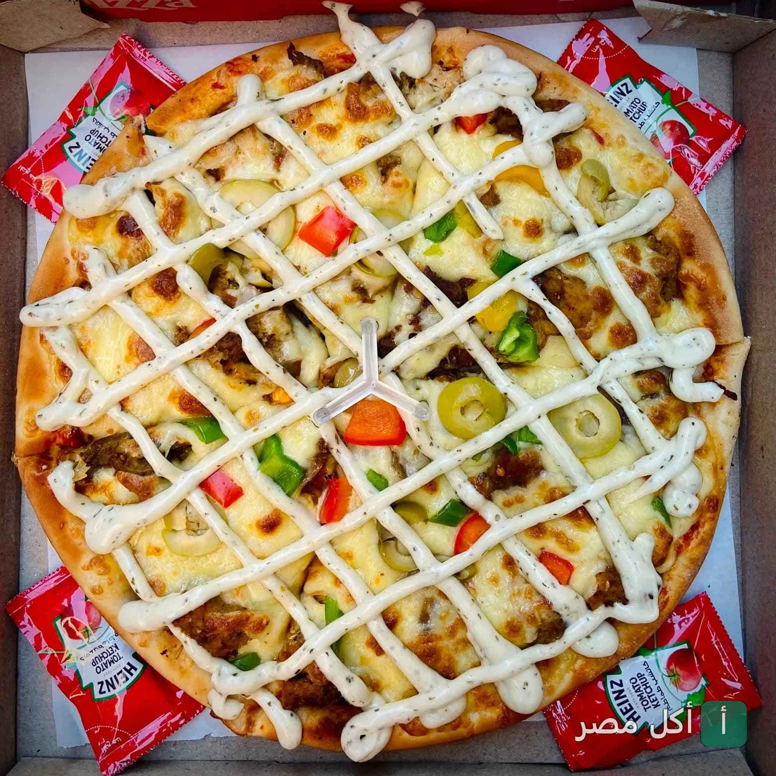 بيتزا ميلانو في السنطة مغطاة بصوص أبيض وفلفل ألوان وزيتون في علبة كرتون مع أكياس كاتشب.
