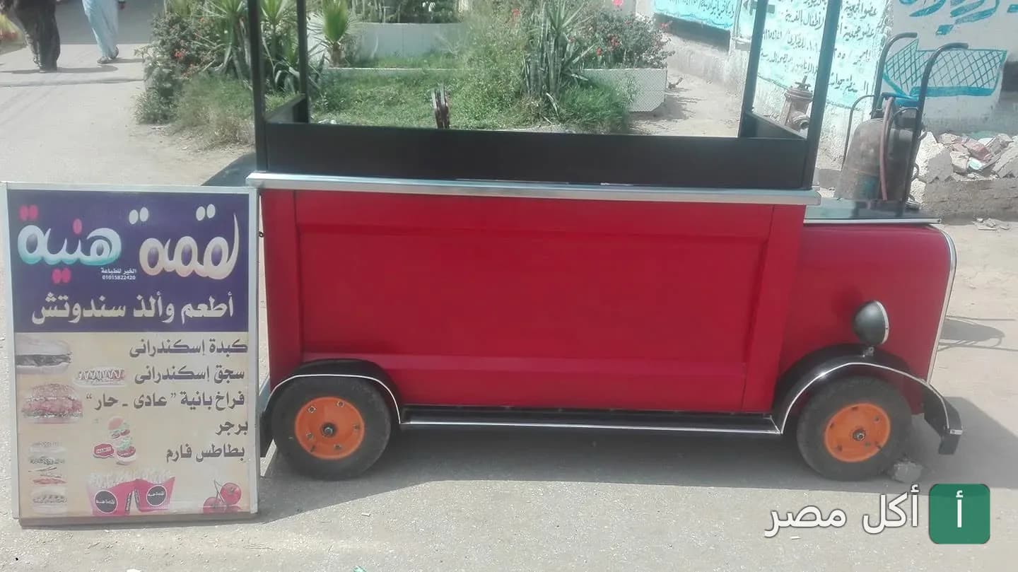 عربة طعام حمراء مميزة لمطعم لقمة هنية في السنطة مع لوحة إعلانية توضح قائمة السندوتشات.