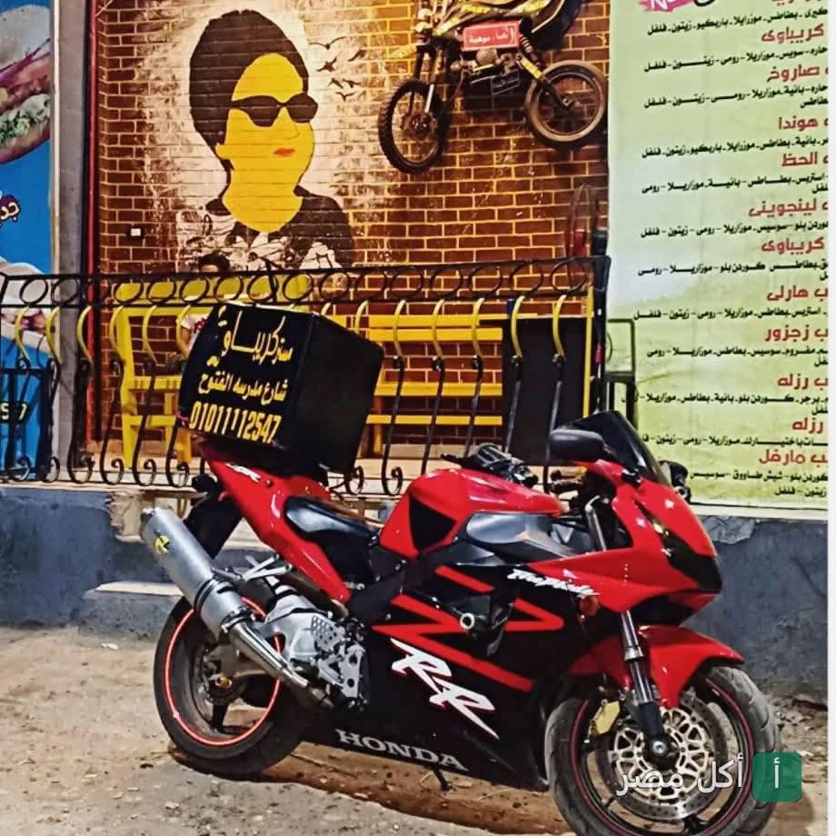 دراجة نارية حمراء مجهزة للتوصيل أمام واجهة مطعم كريباوي في السنطة، الغربية.