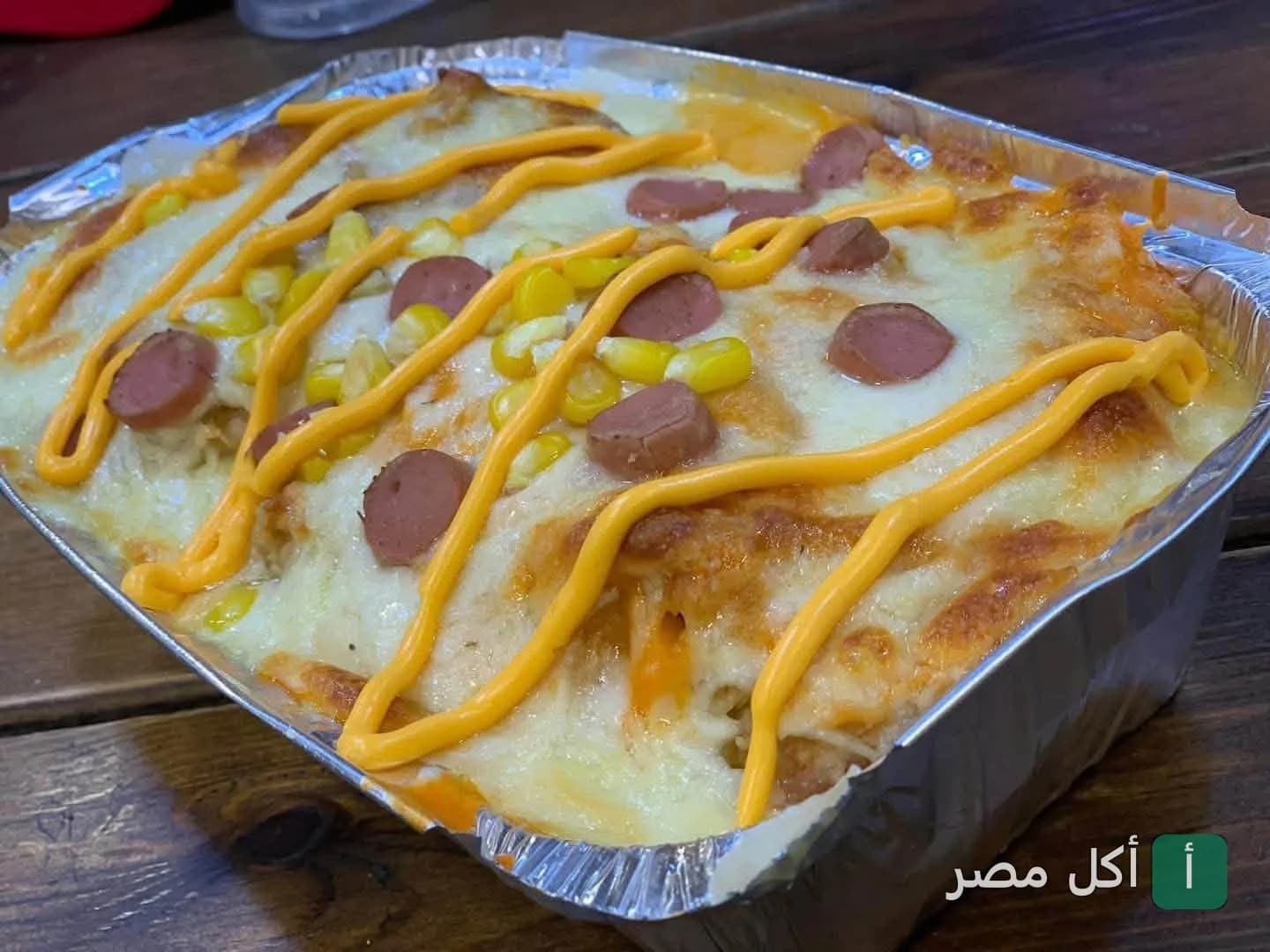 وجبة سريعة في علبة فويل مغطاة بالجبن السايح وقطع السوسيس والذرة من مطعم كريباوي بالسنطة.