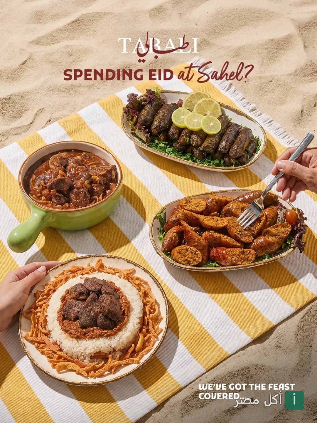 مجموعة أطباق شرقية متنوعة من مطعم طبالي الزمالك، تشمل محشي ورق عنب، سجق، وطاجن لحم، موضوعة على مفرش أصفر وأبيض على رمال الشاطئ.