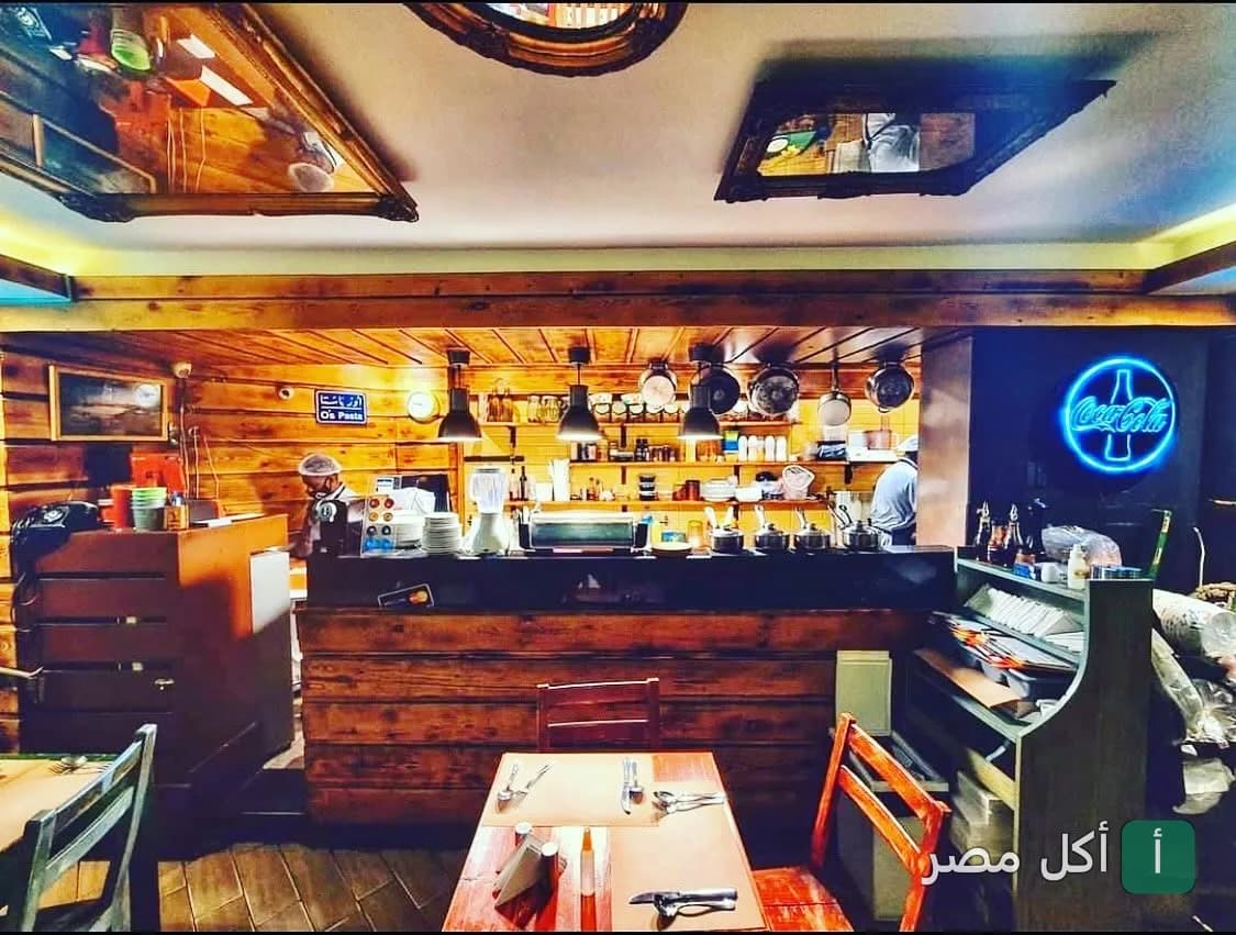 ديكور خشبي دافئ وتصميم داخلي لمطعم أوس باستا في الزمالك مع طاولة طعام ومطبخ مفتوح.