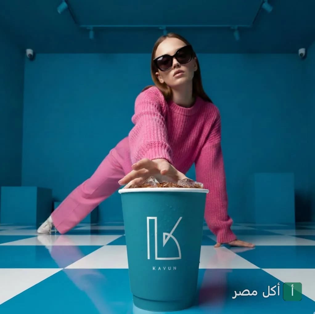 فتاة ترتدي ملابس وردية ونظارة شمسية بجانب كوب مشروب يحمل شعار كافون في الزمالك.