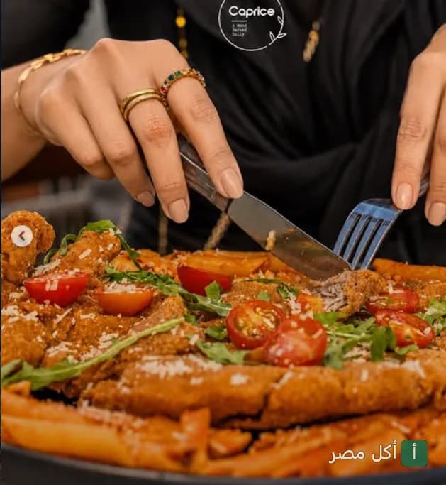 شخص يستخدم السكين والشوكة لتقطيع طبق مكرونة بصوص الطماطم مع قطع الدجاج في مطعم إل كابريس بالزمالك.