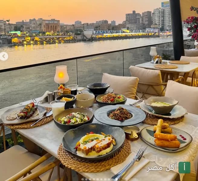 مائدة طعام متنوعة في مطعم رابيندا بالزمالك مع إطلالة مباشرة على النيل وقت الغروب.