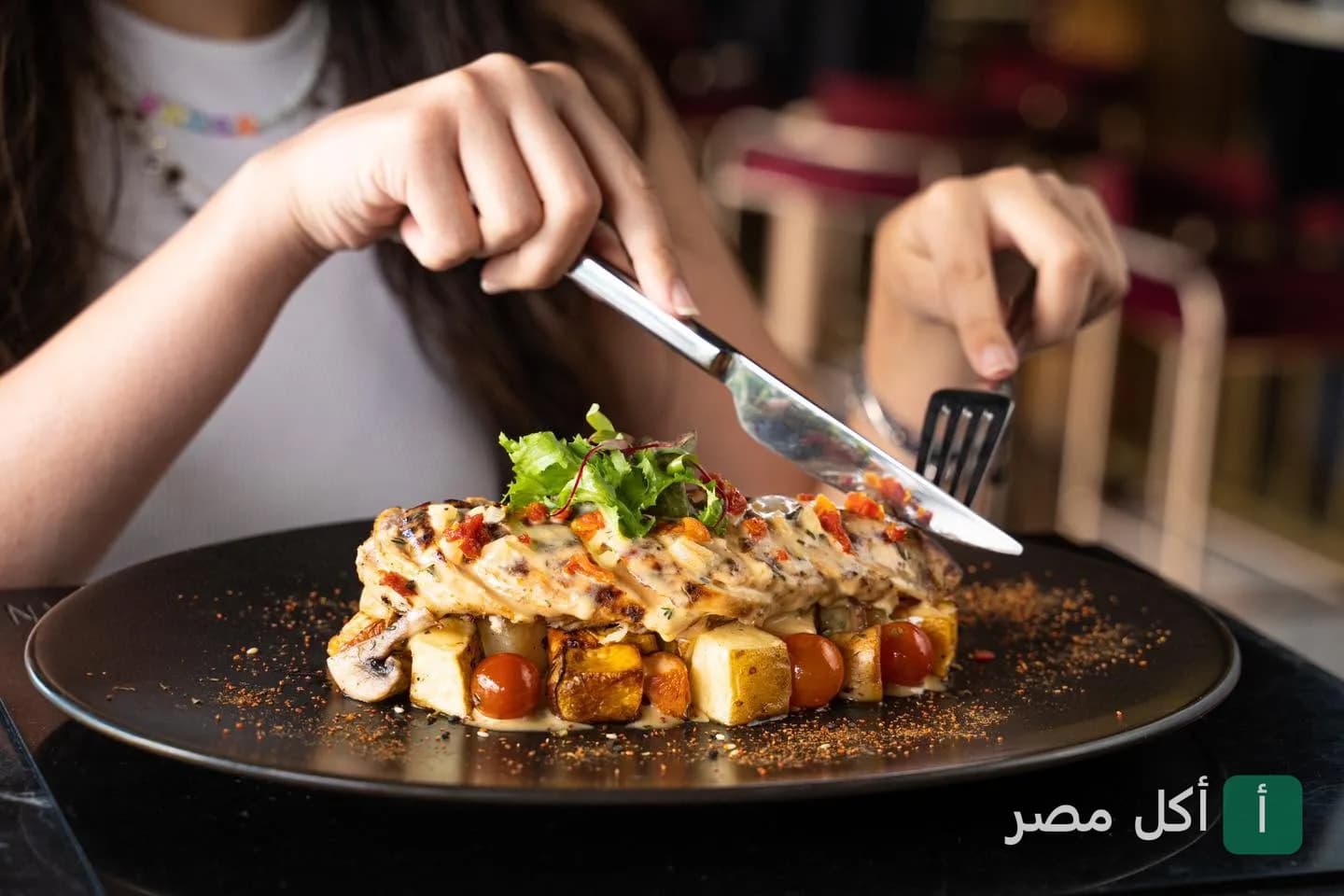 شخص يقطع طبق دجاج مشوي مع خضروات في مطعم كازان بالزمالك.