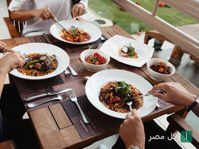 أشخاص يتناولون وجبات متنوعة على طاولة خشبية في مطعم وكافيه إسبلاناد بمصر الجديدة.