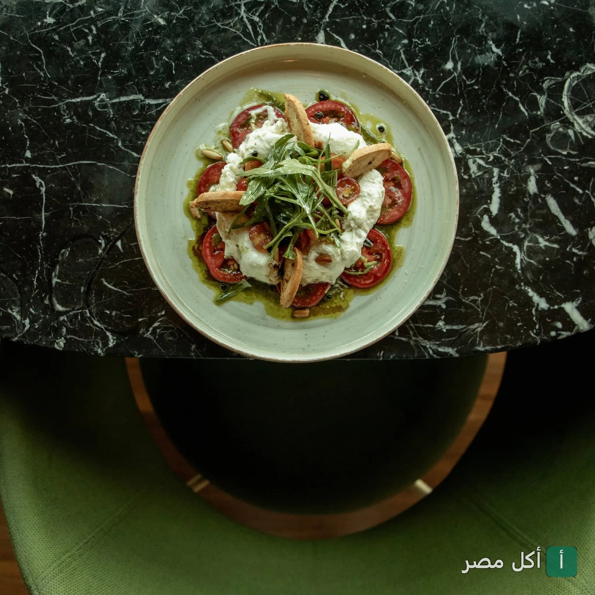 طبق سلطة بوراتا مع الطماطم والجرجير على طاولة رخامية في مطعم ساتشي هليوبوليس بالقاهرة.