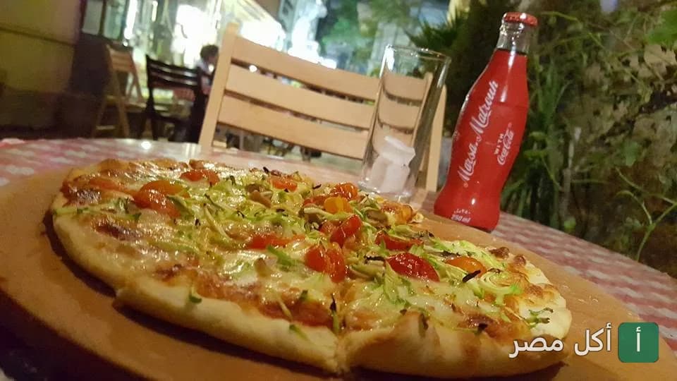 بيتزا بالخضروات على لوح خشبي مع زجاجة كوكاكولا في مطعم كايروما بباب اللوق.