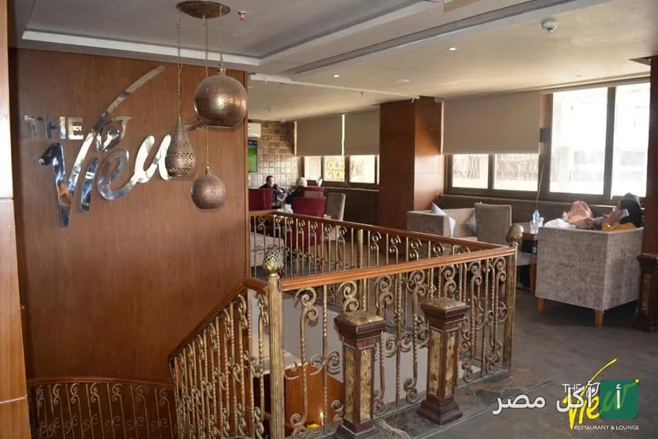 ديكور داخلي وجلسات مريحة في مطعم ذا فيو بالقاهرة مع إضاءة دافئة ودرابزين معدني.