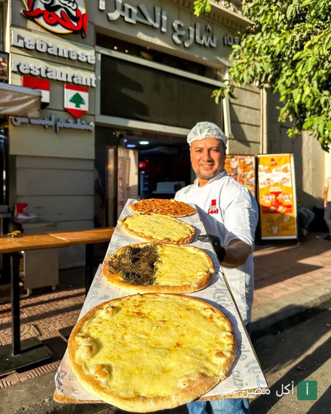شيف مطعم شارع الحمرا في باب اللوق يحمل صينية كبيرة عليها أنواع مختلفة من المعجنات الشرقية أمام واجهة المطعم.