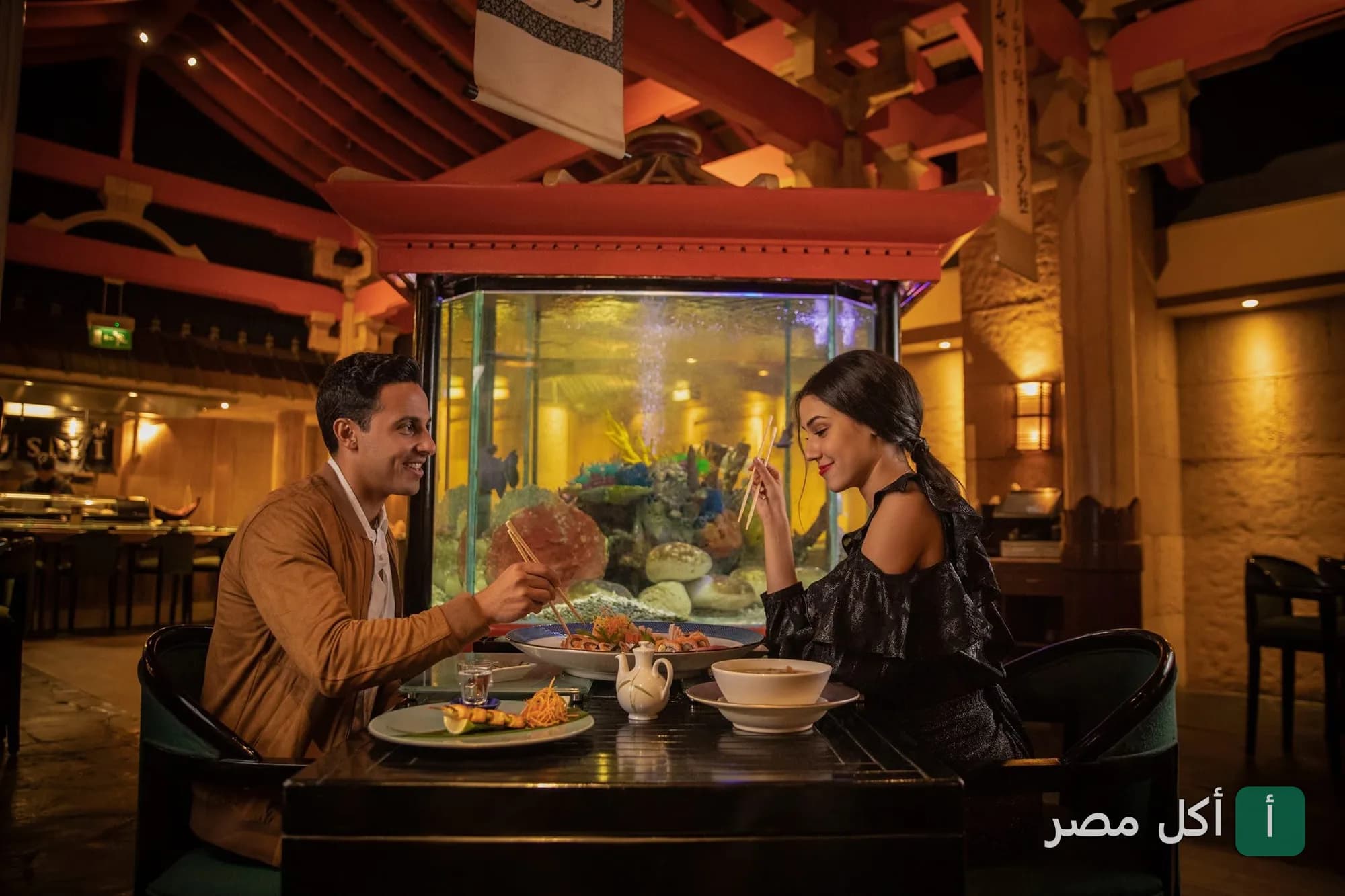 زوجان يتناولان الطعام في مطعم شوجان بمصر الجديدة، القاهرة، مع ديكور ياباني وحوض أسماك كبير.