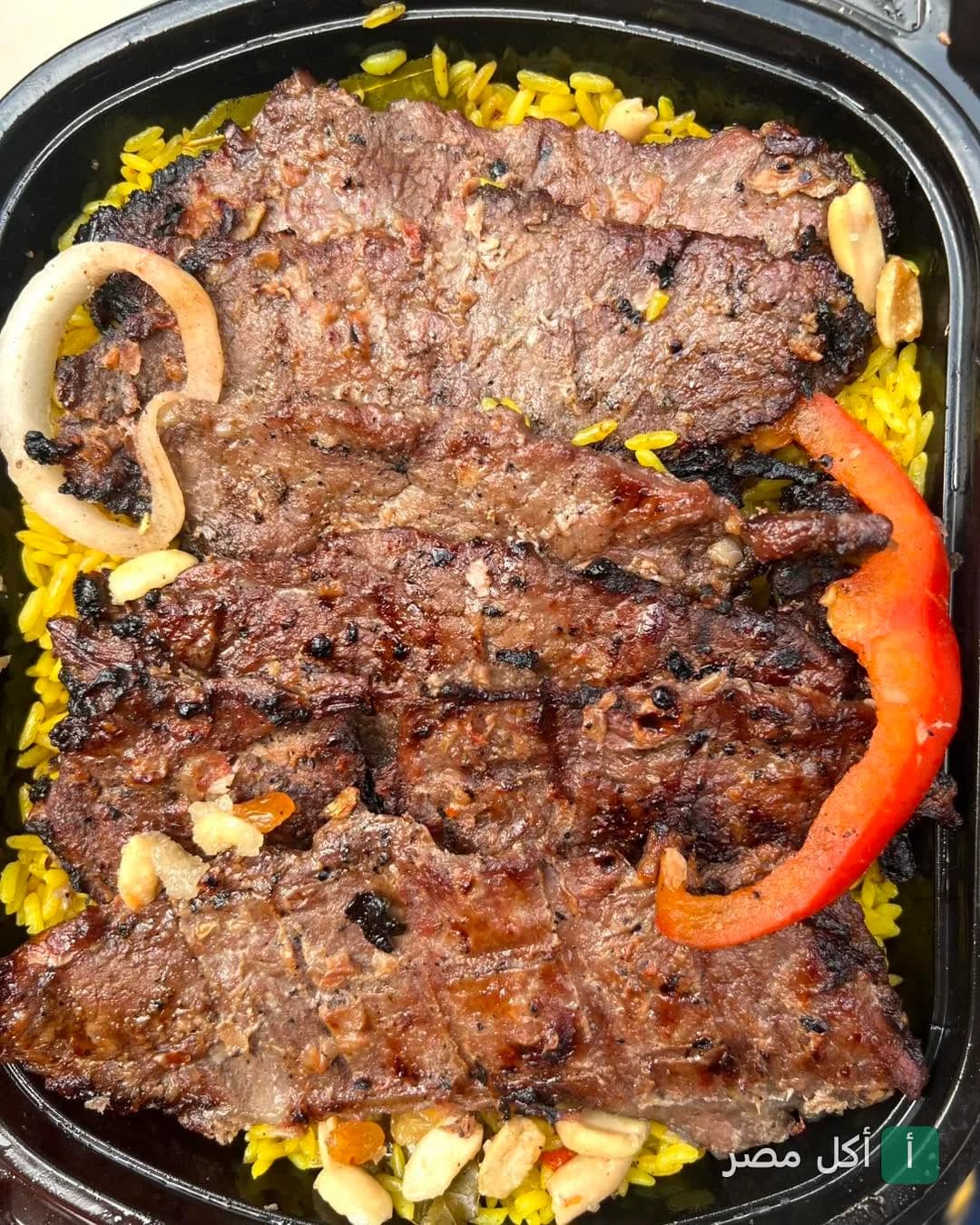 طبق مشويات كبابجي أبو حمادة في بولاق الدكرور، شرائح لحم مشوي على أرز أصفر بالمكسرات.