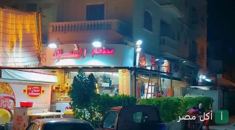 واجهة مطعم الشعلان في 6 أكتوبر ليلاً مع لافتة مضيئة وأشجار زينة.