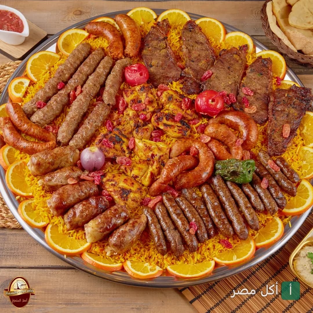 صينية مشويات مشكلة من حضرموت والسمار في 6 أكتوبر تضم كفتة، سجق، وقطع لحم على أرز مبهر مزينة بشرائح البرتقال.