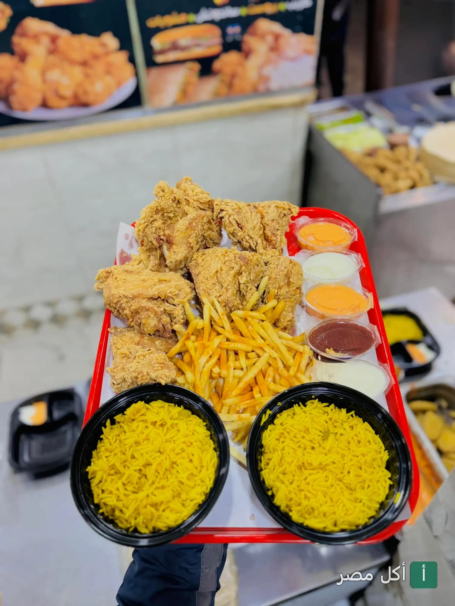 صينية تحتوي على قطع دجاج مقلي مقرمش، بطاطس محمرة، وأطباق أرز أصفر مع صوصات متنوعة في مطعم عرب بني صالح بأطفيح.