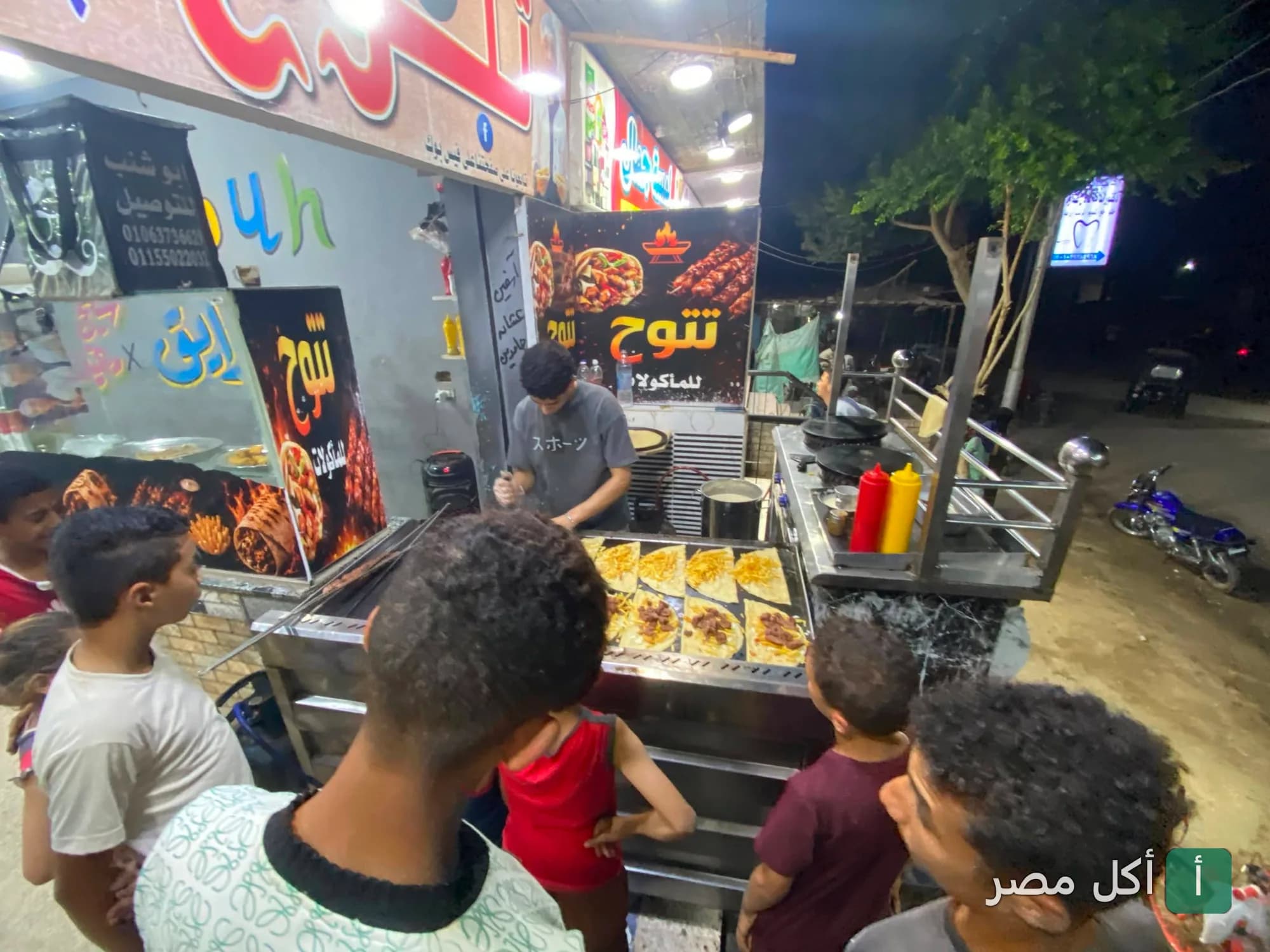 طباخ يحضر الساندوتشات على الصاج أمام مطعم تتوح في أطفيح وسط تجمع من الزبائن.