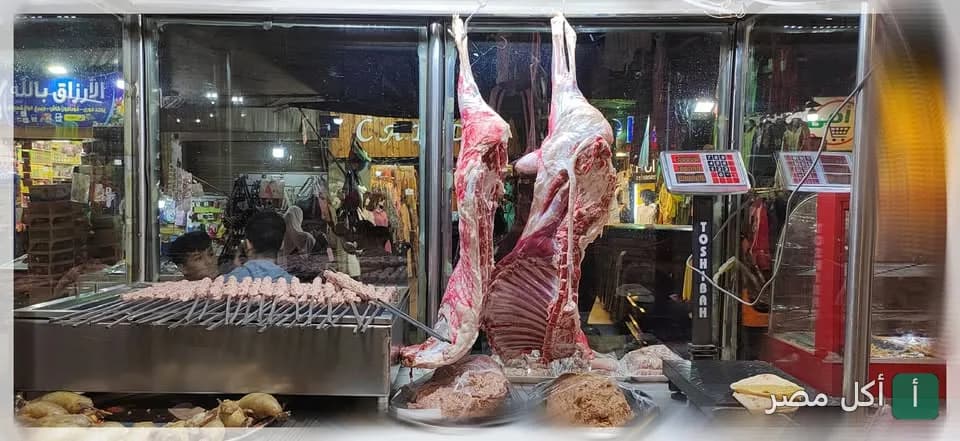 واجهة مطعم عبدين في أطفيح تعرض ذبائح معلقة وأسياخ كفتة طازجة على الشواية.