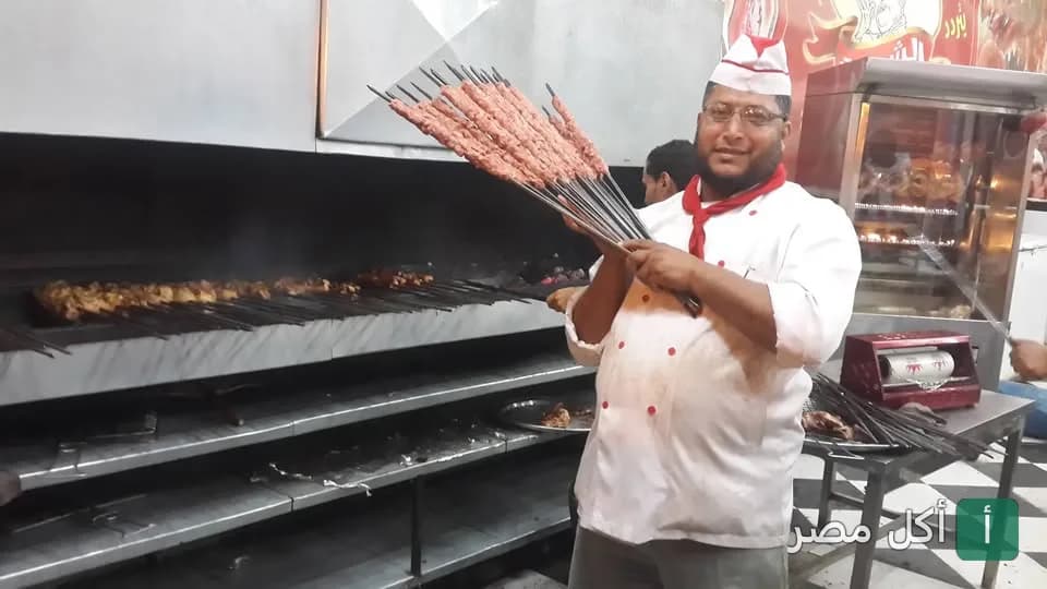 شيف كبابجى الشيخ في أطفيح يحمل أسياخ الكفتة النيئة أمام شواية الفحم.