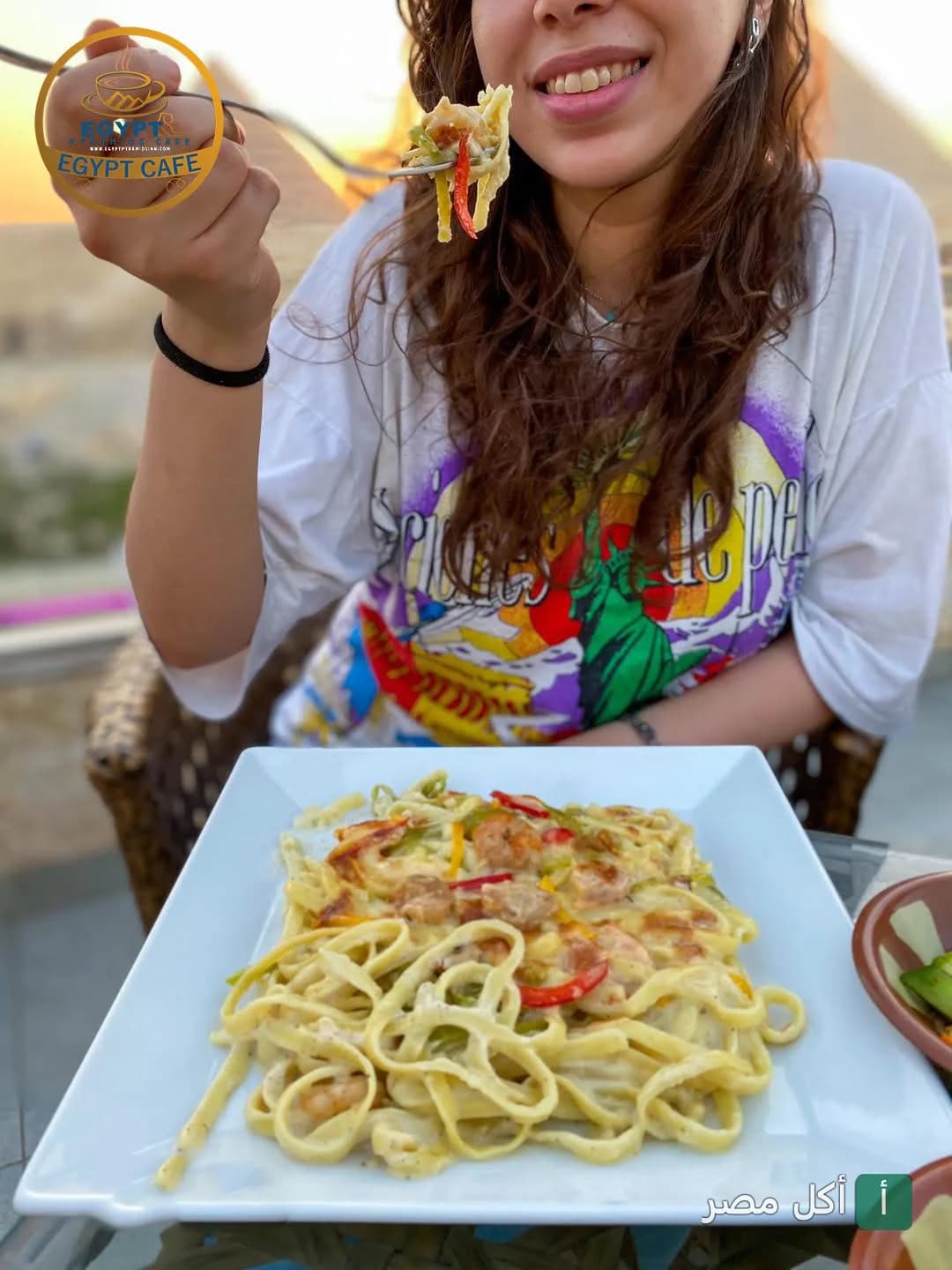 زبونة تتناول طبق مكرونة بالجمبري في مطعم بيراميدز مع إطلالة على الأهرامات.