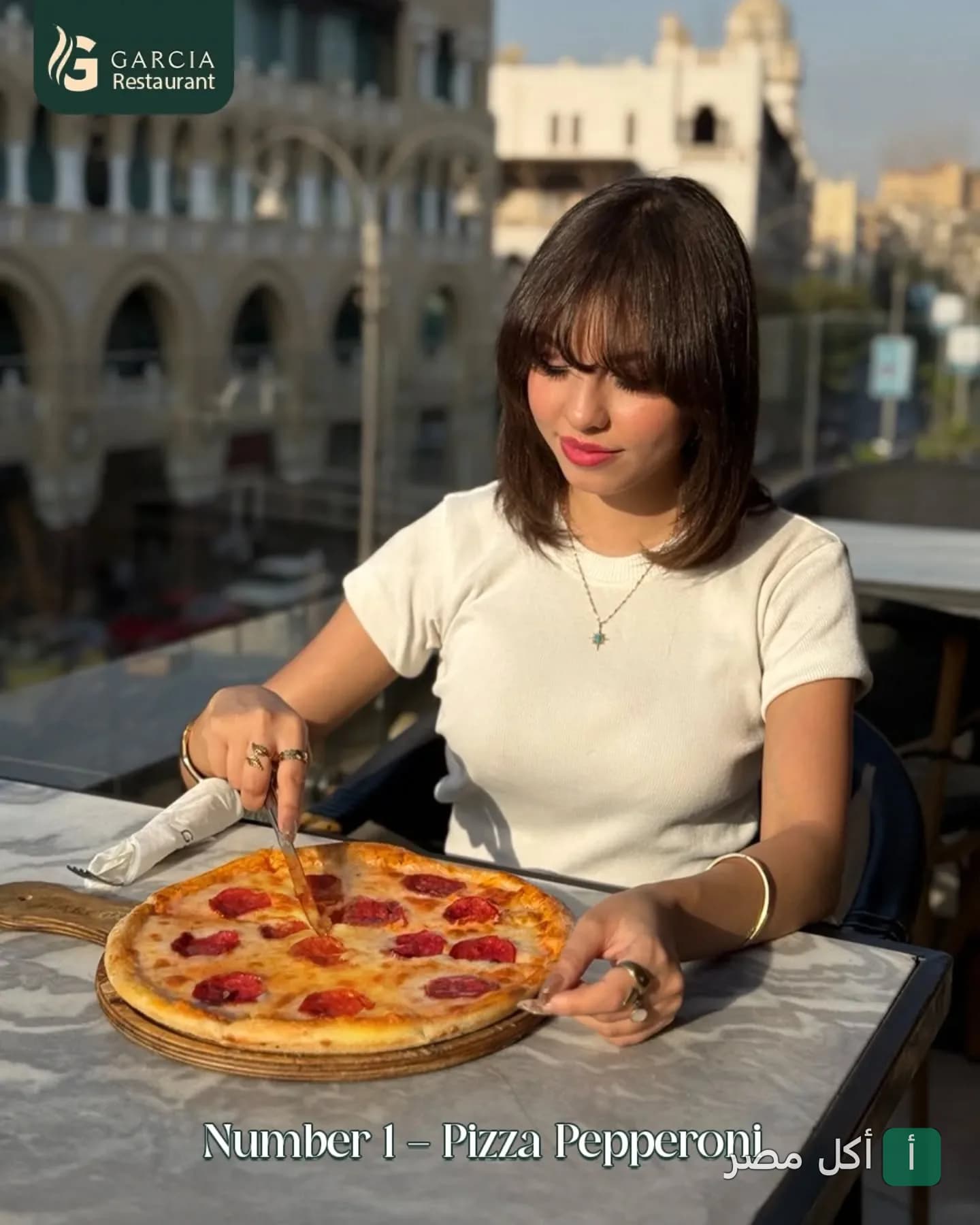 فتاة تقطع بيتزا بيبيروني على طاولة في تراس غارسيا راستوران اند كافيه.