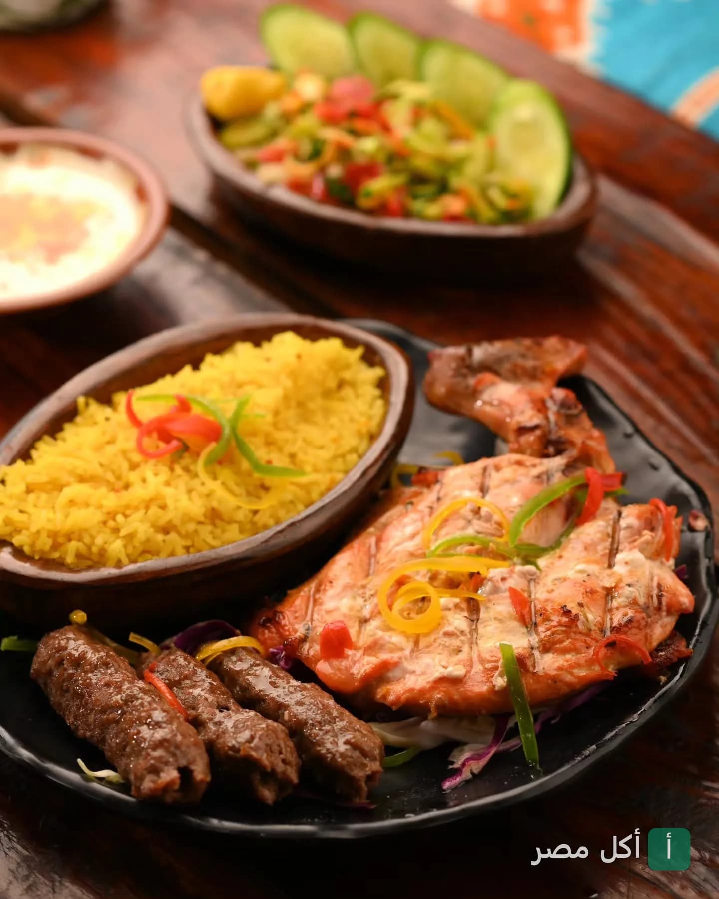 طبق مشويات متنوع من مطعم الكوخ يضم دجاج مشوي وكفتة مع أرز أصفر وسلطة خضراء.