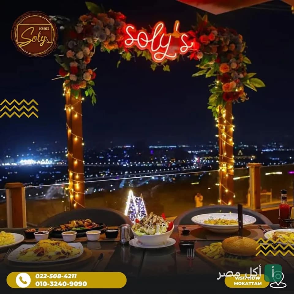 طاولة طعام في مطعم سولي بالمقطم مع إطلالة ليلية مميزة وديكور زهور ونيون