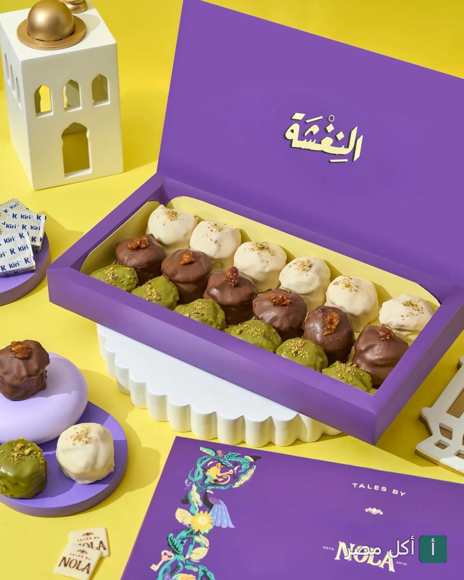 علبة حلويات نولا كوربة الأرجوانية تحتوي على تشكيلة متنوعة من الكب كيك المغطى بالشوكولاتة والمكسرات.