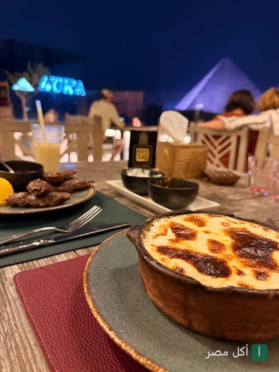 طاجن مصري على طاولة في مطعم زيارة بيراميدز إيليت مع إطلالة ليلية على الأهرامات.