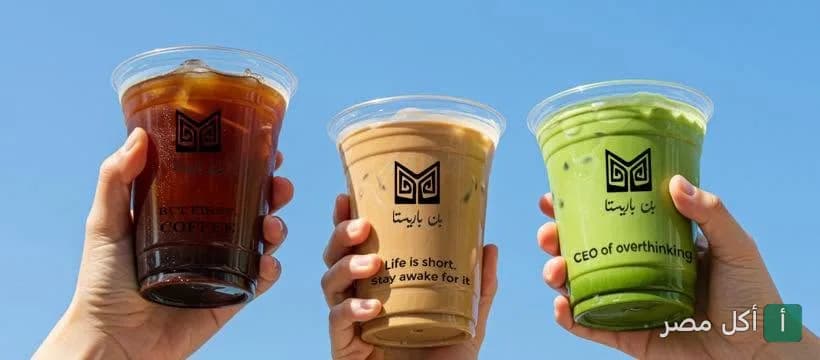 ثلاثة أكواب قهوة مثلجة وماتشا من باريستا كافيه في مصر الجديدة مرفوعة أمام سماء صافية.
