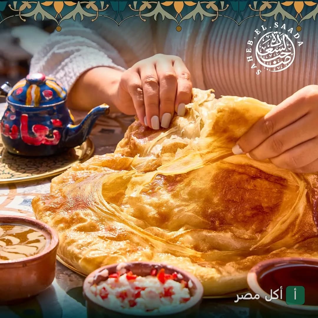 شخص يقطع فطير مشلتت طازج في مطعم صاحب السعادة مع إبريق شاي ملون وأطباق جانبية.
