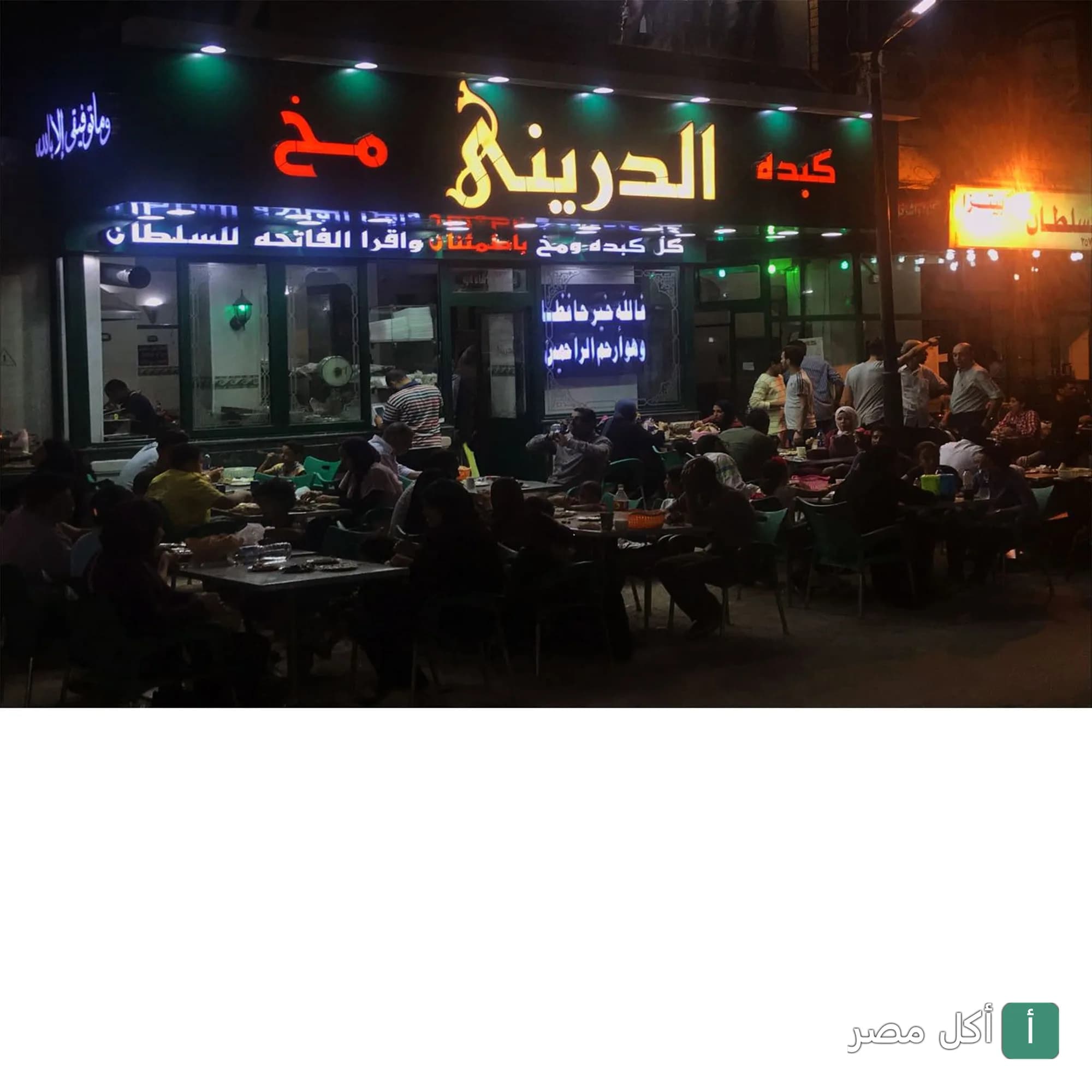 واجهة مطعم كبده ومخ الدريني في جزيرة إمبابة ليلاً مع زبائن يجلسون في الخارج.