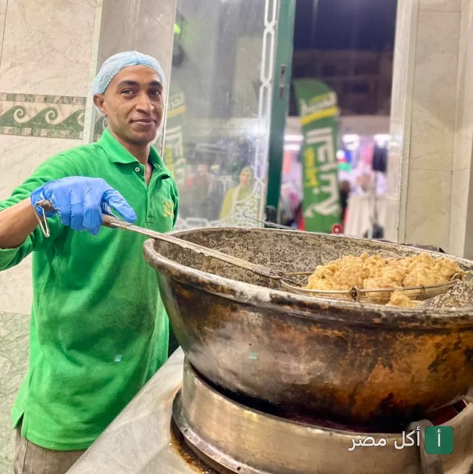 طباخ يرتدي زي أخضر في مطعم كبده ومخ الدريني بجزيرة إمبابة يقوم بقلي الطعام في مقلاة كبيرة.