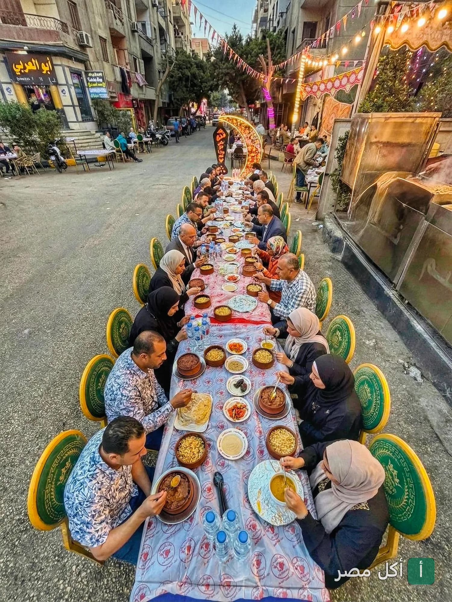 مائدة إفطار رمضانية طويلة في الشارع أمام مطعم وجزارة نجم في إمبابة.