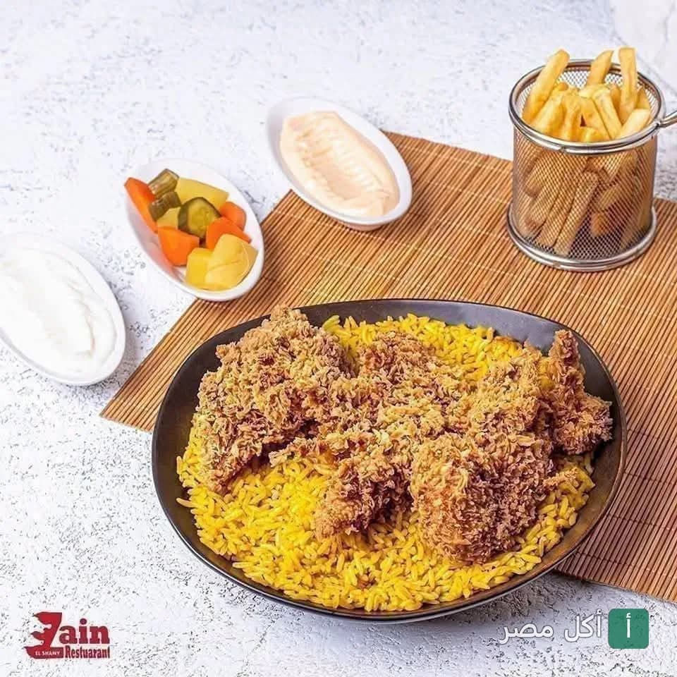 طبق أرز أصفر مع قطع دجاج مقرمشة، يقدم مع بطاطس مقلية ومقبلات في مطعم زين الشام بإمبابة.