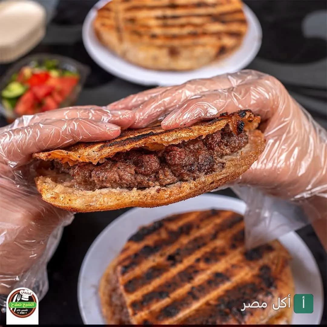 شخص يمسك رغيف حواوشي مشوي من مطعم الشيخ صلاح الكبابجي في إمبابة.
