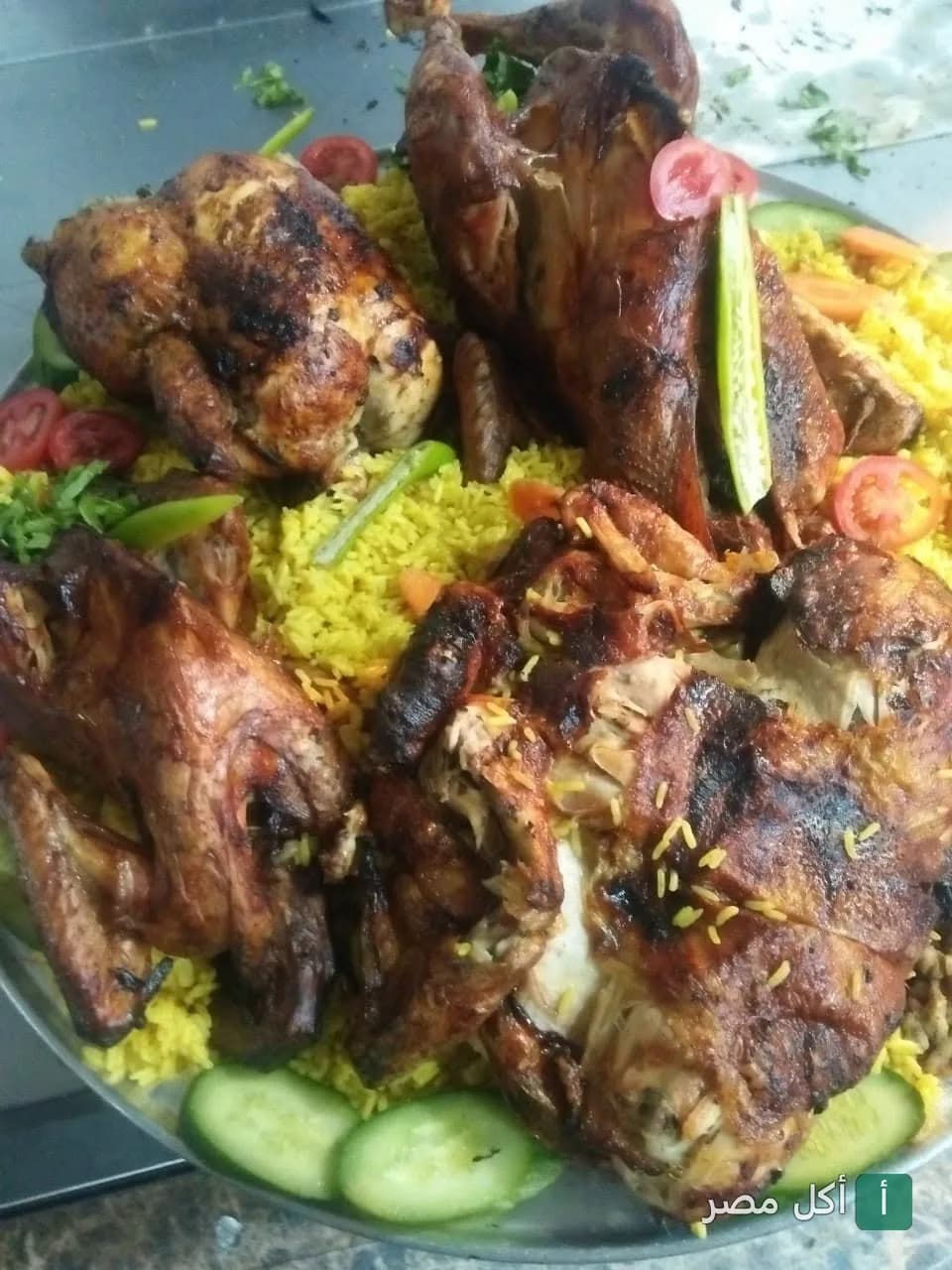 طبق كبير من الفراخ المشوية على الأرز الأصفر المزين بشرائح الخيار والطماطم من مشويات أبواليزيد في إمبابة.