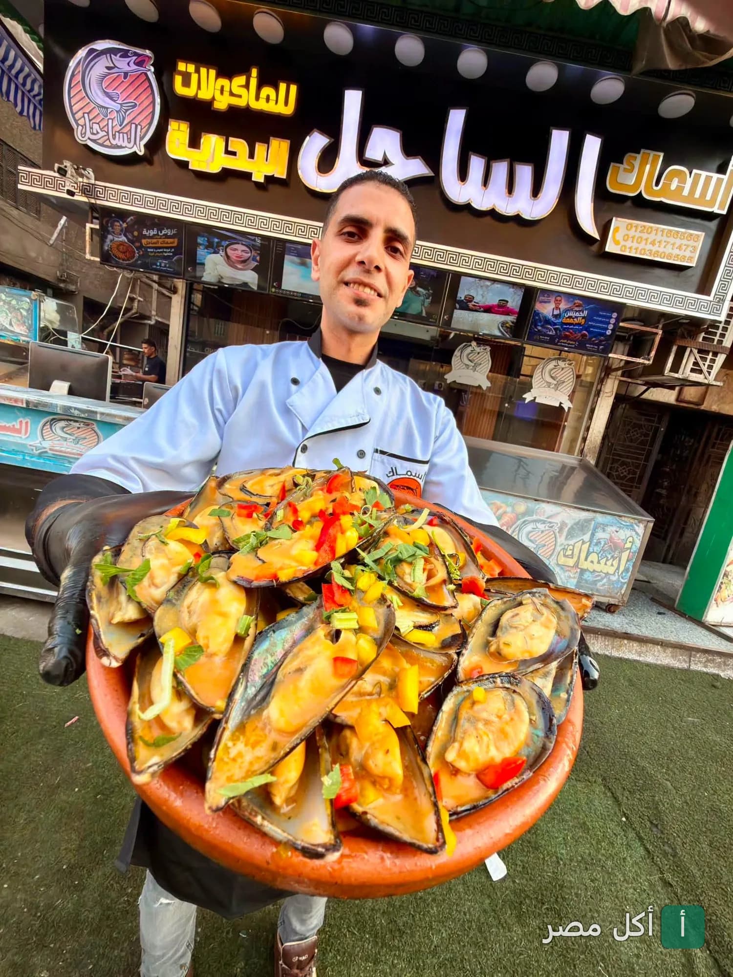 شيف مطعم اسماك الساحل في إمبابة يقدم طبق بلح البحر الطازج أمام واجهة المطعم.