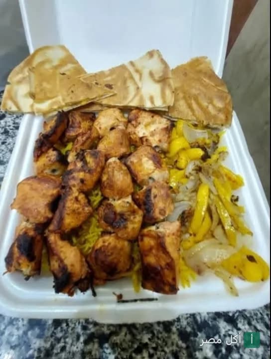وجبة شيش طاووق مع أرز أصفر وفلفل ألوان وخبز في علبة تيك أواي من مطعم التاج السوري بإمبابة.