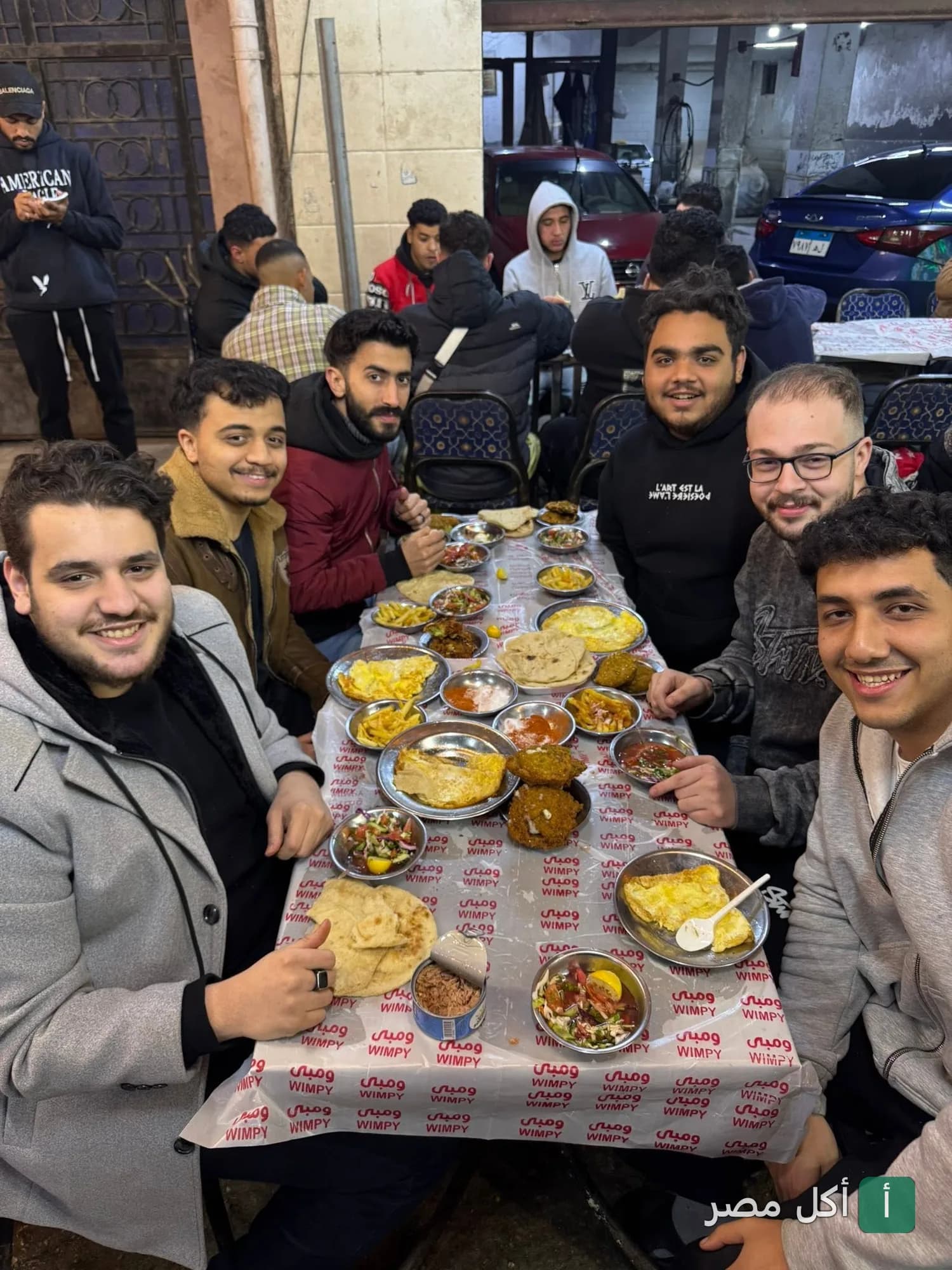 مجموعة من الشباب يتناولون وجبة إفطار شرقي متنوعة على مائدة في مطعم فول وفلافل نيو ومبى بإمبابة.