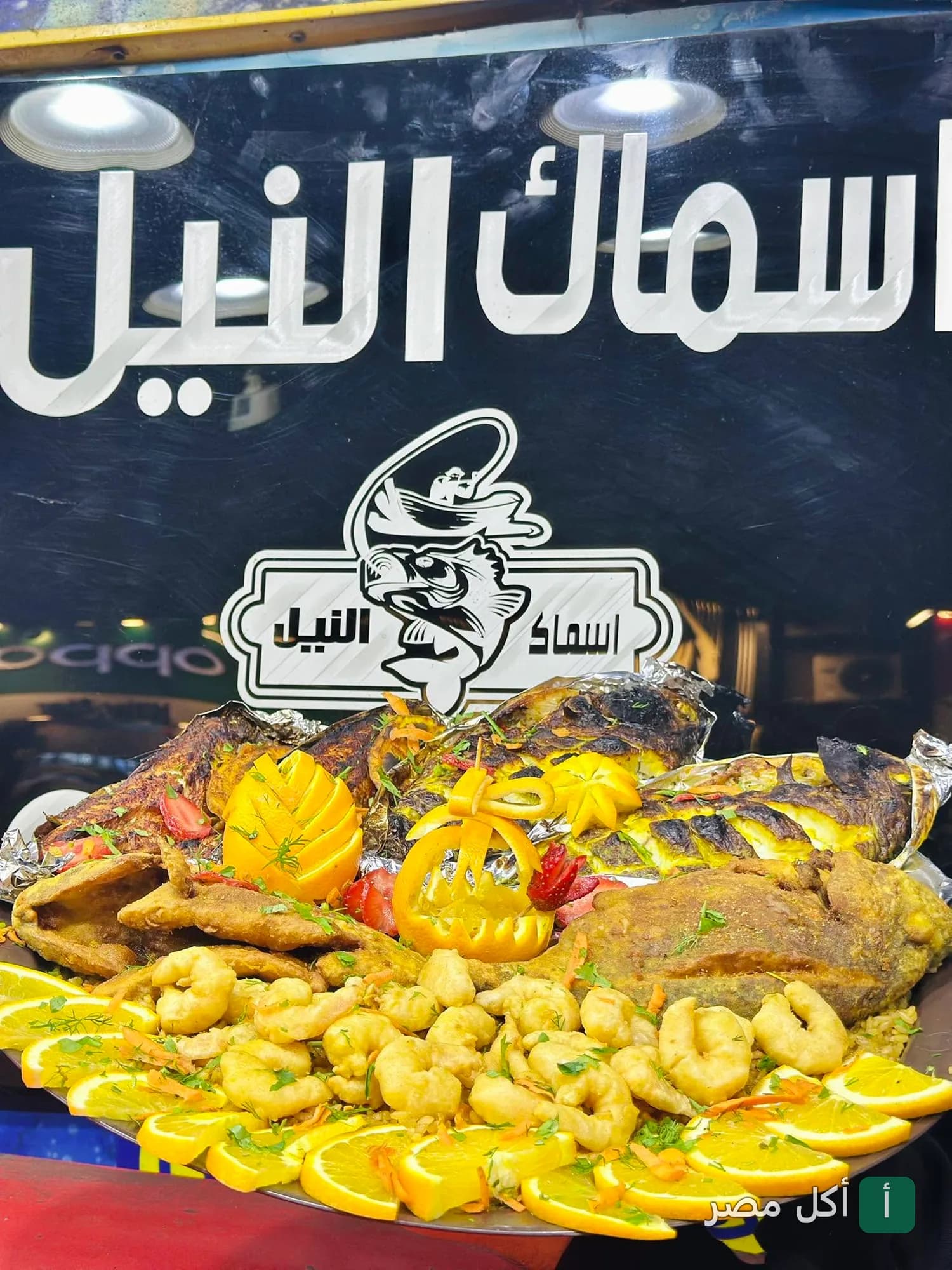 طبق مأكولات بحرية متنوعة أمام لوحة مطعم اسماك النيل في بشتيل بإمبابة.