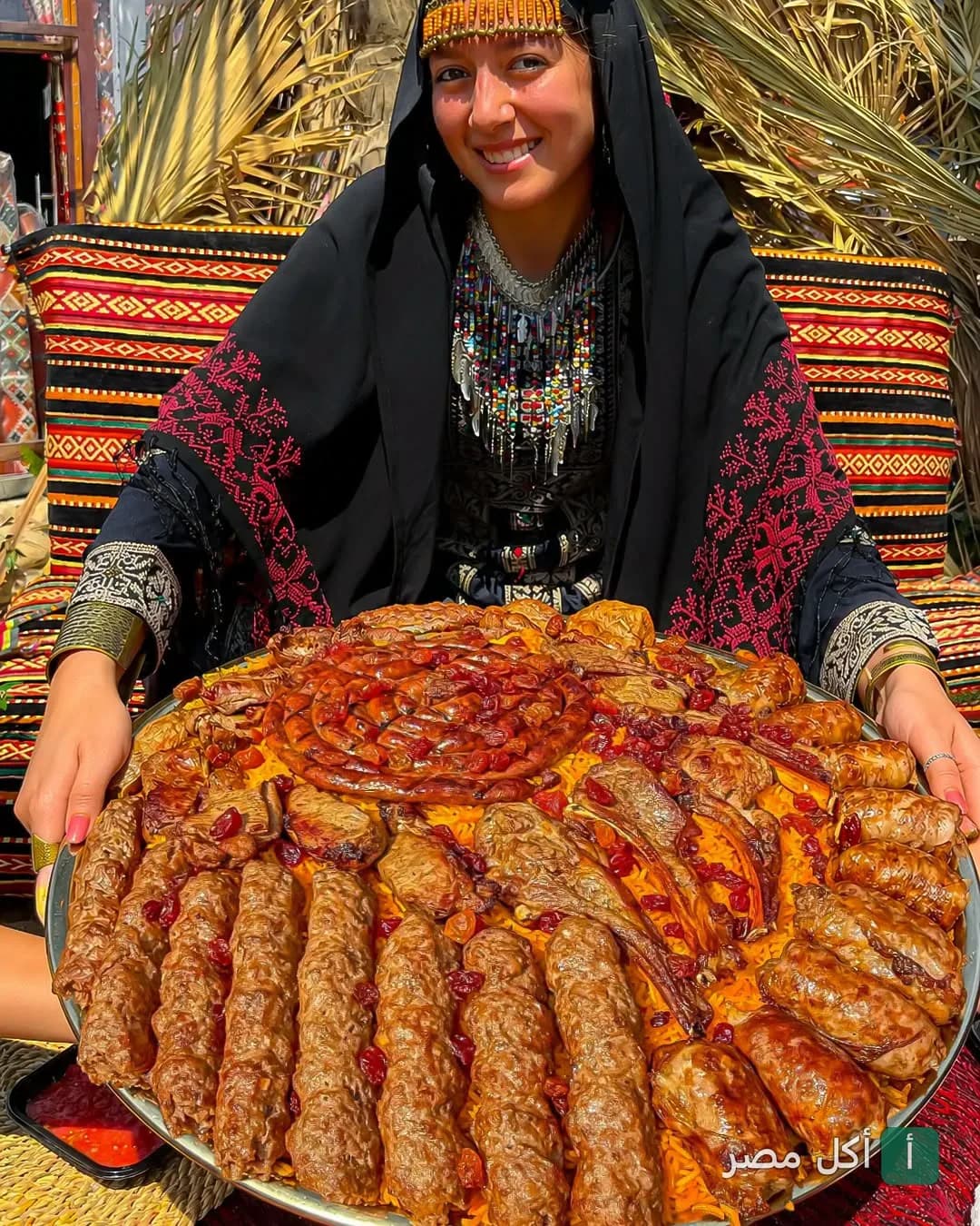فتاة ترتدي زيًا تراثيًا تقدم صينية كبيرة من المندي والمشويات في مطعم حضرموت شيخ المندي بالشيخ زايد.