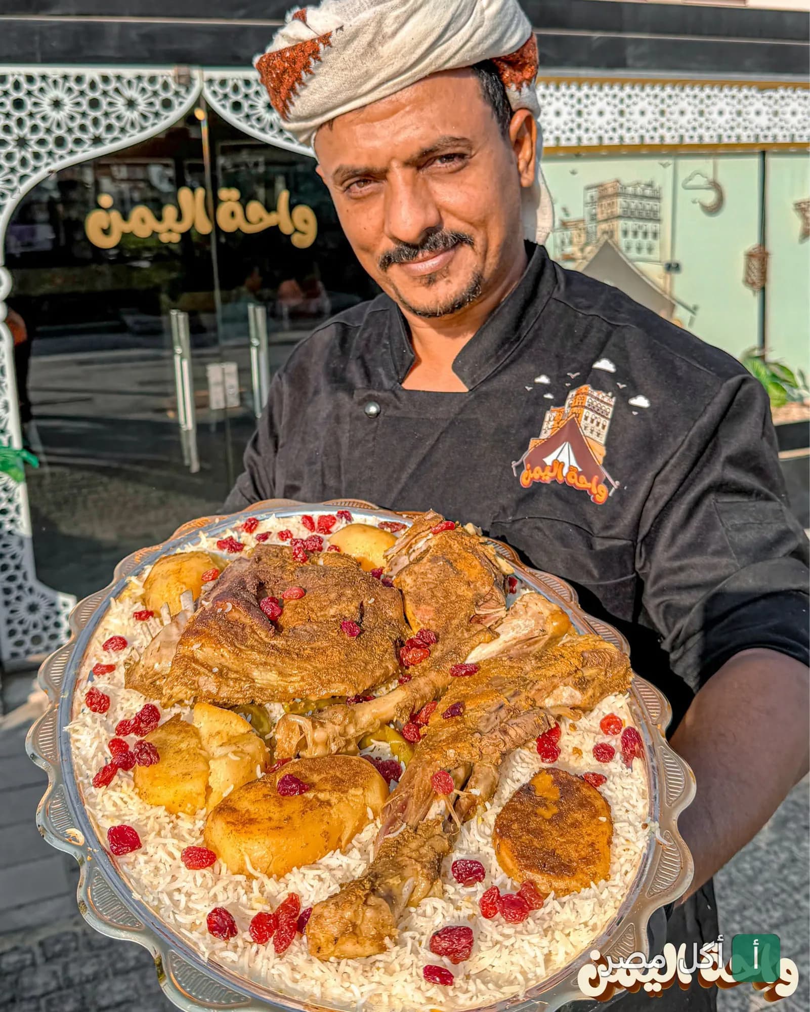 شيف مطعم واحة اليمن في الشيخ زايد يقدم طبق أرز شرقي باللحم أمام واجهة المطعم.