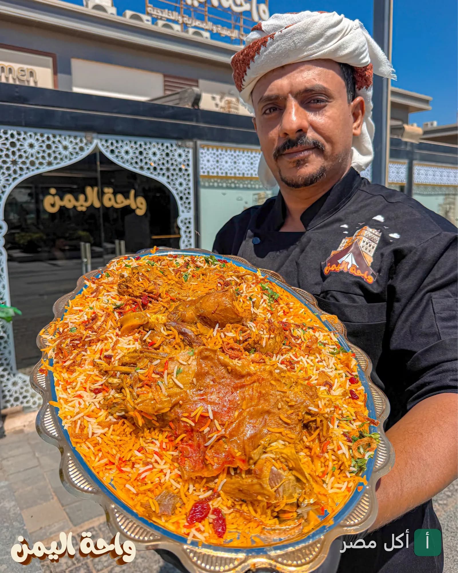 شيف مطعم واحة اليمن في الشيخ زايد يقدم طبق أرز شرقي كبير أمام واجهة المطعم.