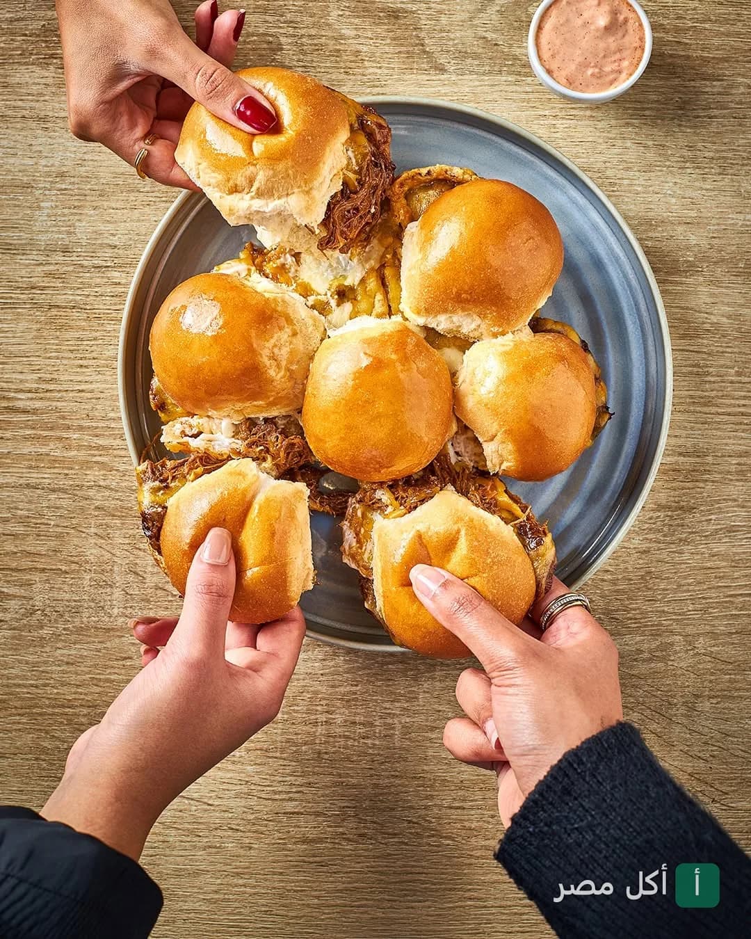 أيدي أشخاص يشاركون طبق سلايدرز برجر في مطعم قهوة بأركان بلازا، الشيخ زايد.