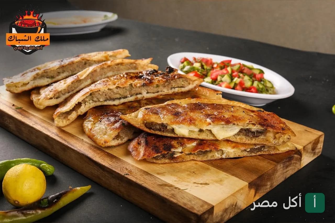 حواوشي بلدي محشو باللحم والجبنة على لوح تقطيع خشبي في مطعم مشويات ملك الشباك بالشيخ زايد.