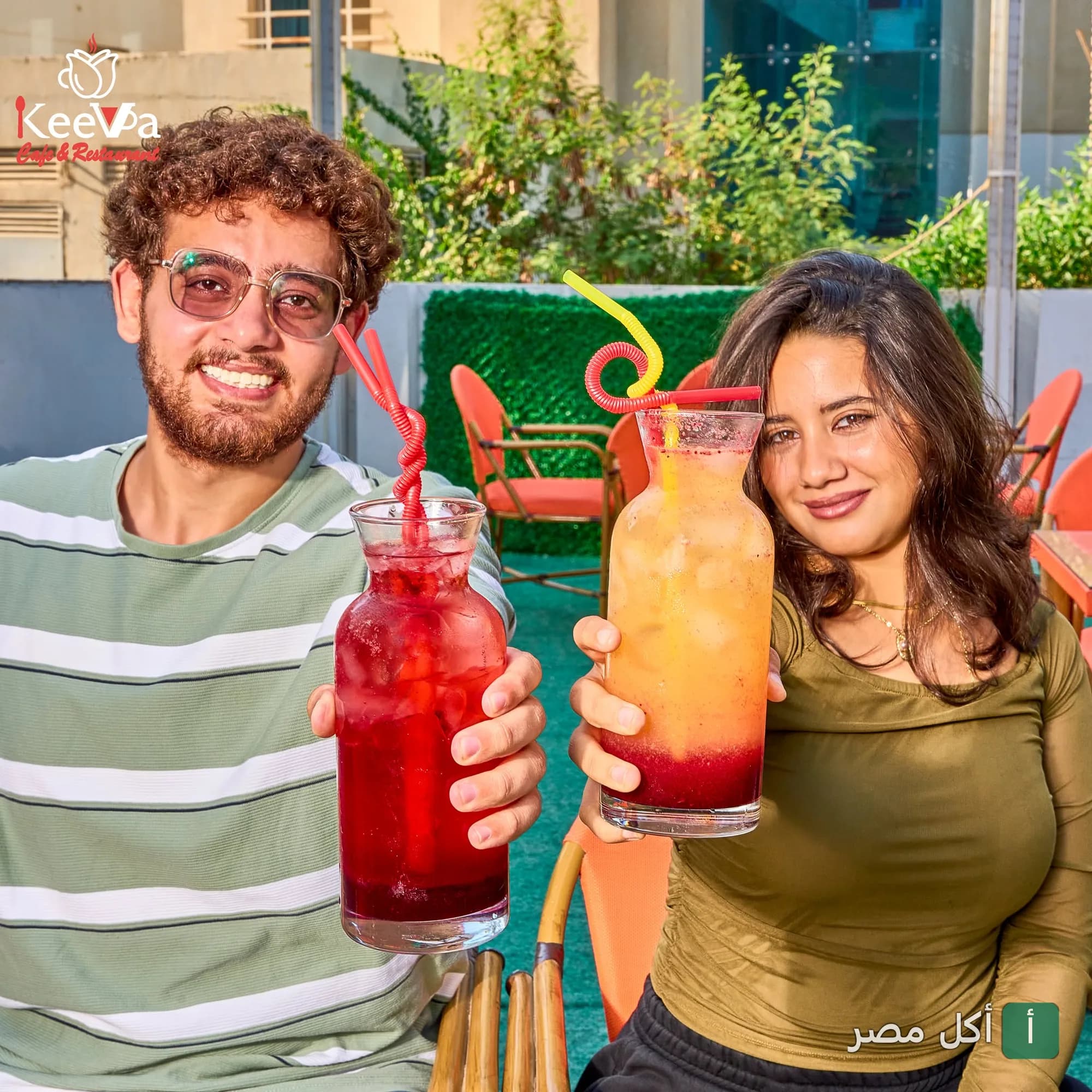 شاب وفتاة يرفعان مشروبات ملونة في جلسة خارجية بكيفا كافيه في داون تاون الشيخ زايد